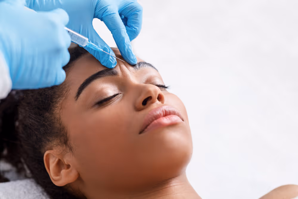 Close-up of a woman receiving a cosmetic injection in the forehead from a medical professional wearing blue gloves.