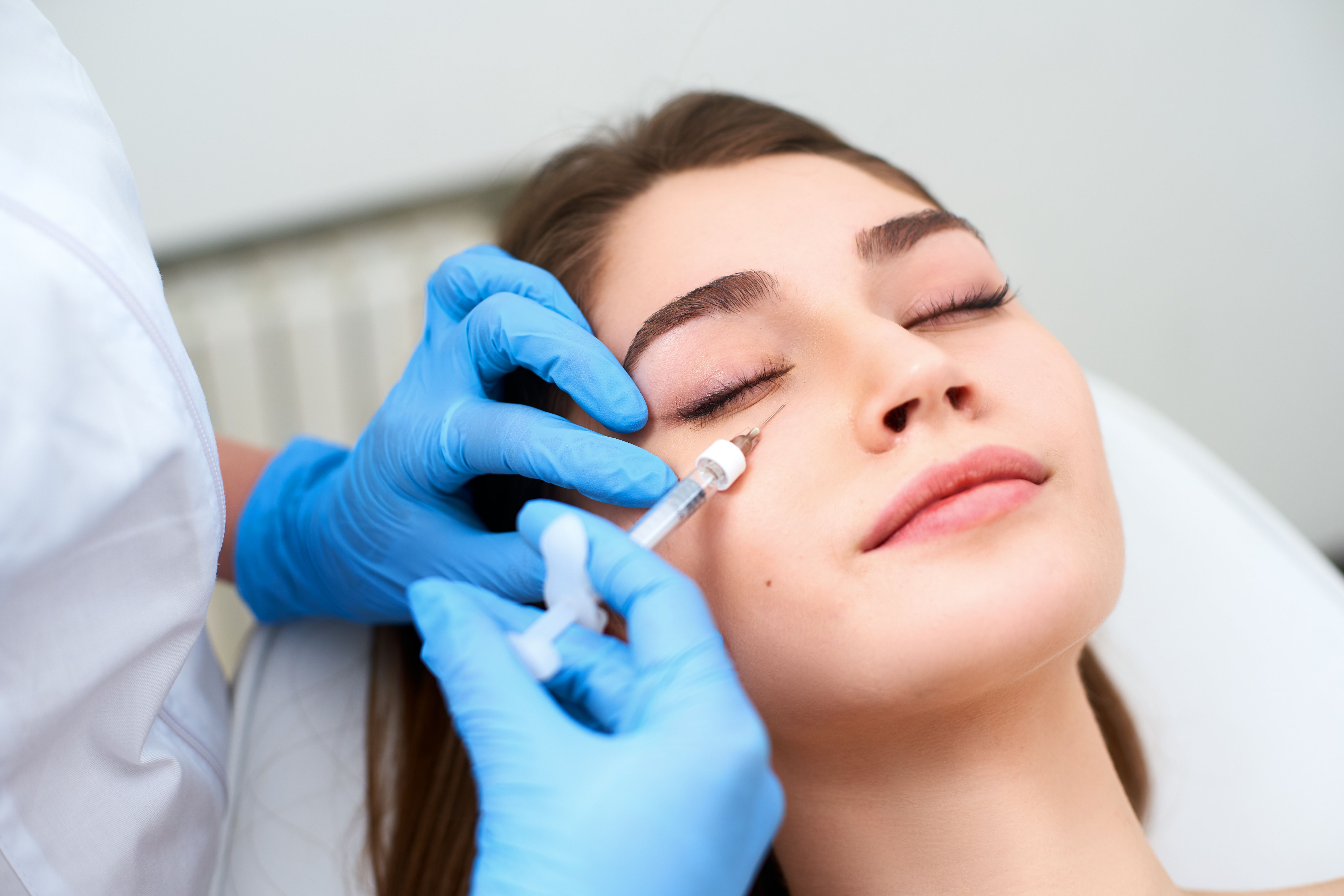 Close-up of a woman receiving a cosmetic injection near her eye from a medical professional wearing blue gloves.