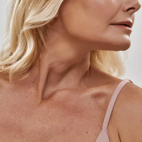 Close-up of a mature woman’s neck, shoulder, and lower face with blonde hair and a pink sleeveless top.