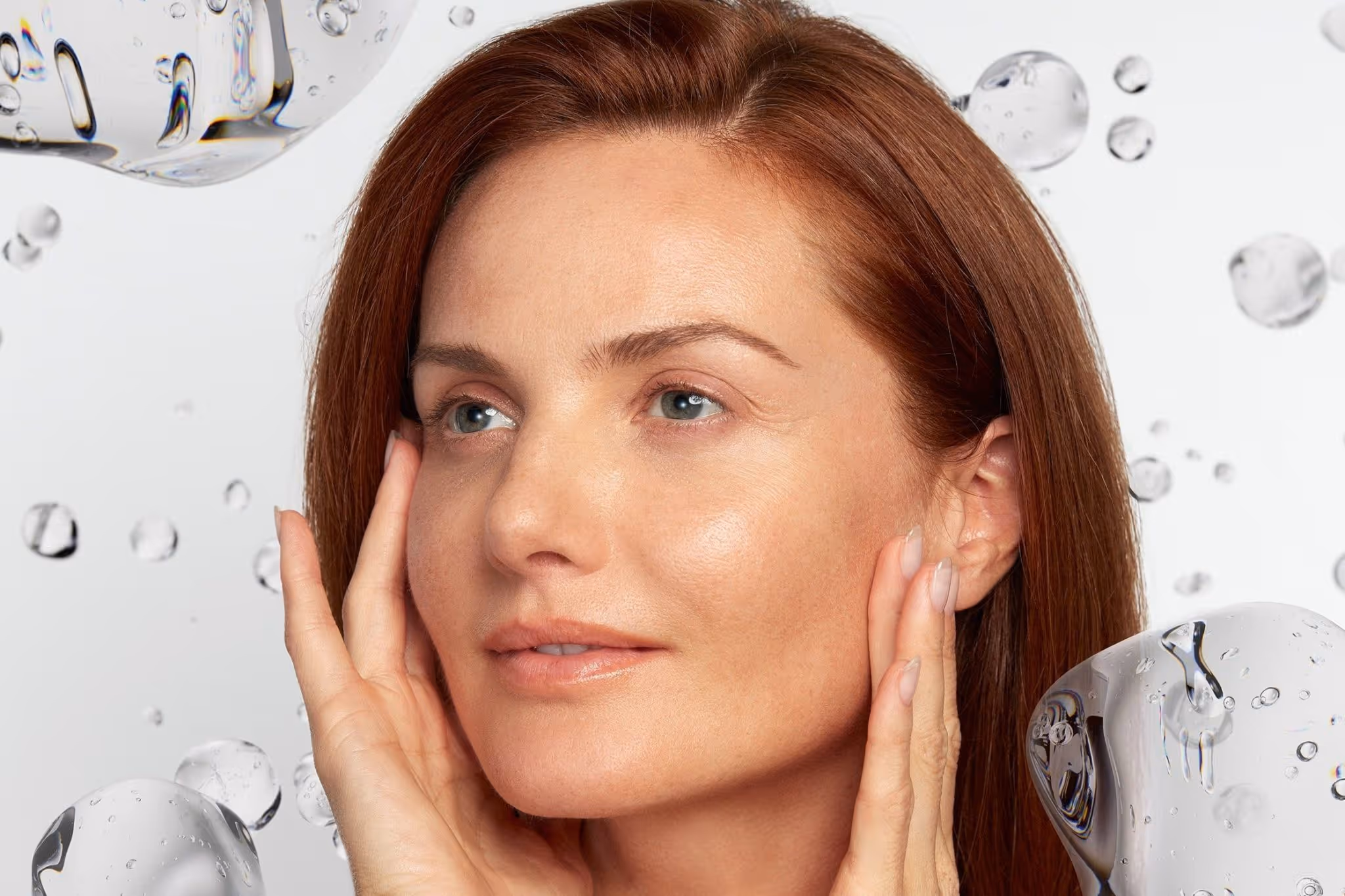 Close-up of a woman with smooth skin touching her face surrounded by clear water-like bubbles.